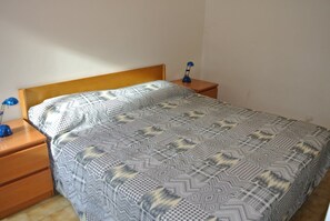 Um quarto com colcha estampada, cabeceira de madeira, duas mesas de cabeceira com abajures e piso de madeira.