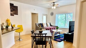 A modern living room with a dining area, a sofa, a TV, and a window with blinds. - Medical center 2-bedroom apartment in perfect Houston with cool AC and comfort (Houston)