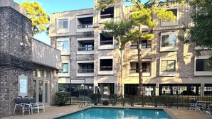 A swimming pool with a 'NO DIVING' sign, surrounded by a brick building with multiple balconies and a clear sky. - Medical center 2-bedroom apartment in perfect Houston with cool AC and comfort (Houston)