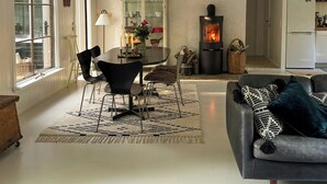 Een woonkamer met een open haard, een eethoek met stoelen en een tafel, en een keuken met een koelkast.