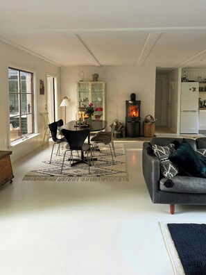 Ein Wohnzimmer mit Kamin, ein Essbereich mit Stühlen und Tisch sowie eine Küche mit Kühlschrank.