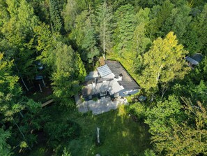 Ein Haus, umgeben von dichtem Wald, mit sichtbarer Garage und einem großen, geneigten Dach.