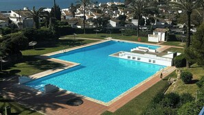 A rectangular swimming pool with a clear blue water, surrounded by a paved deck, and a view of a coastal town with houses and palm trees. - Designer duplex facing the sea in Estepona (Estepona)