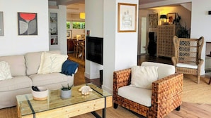 A living room with a sofa, a glass coffee table, a wicker armchair, and a TV. - Designer duplex facing the sea in Estepona (Estepona)
