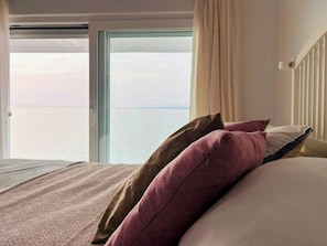 Ein Hotelzimmer mit Bett, einem Fenster mit Vorhängen und Blick auf den Himmel.