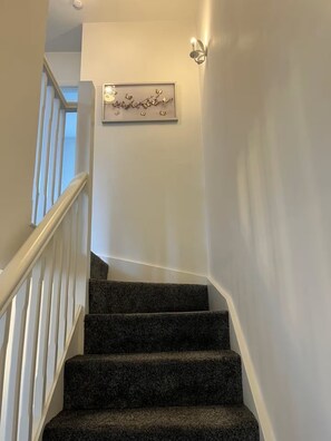 Een trap met beklede treden, witte leuningen en een wandlamp.