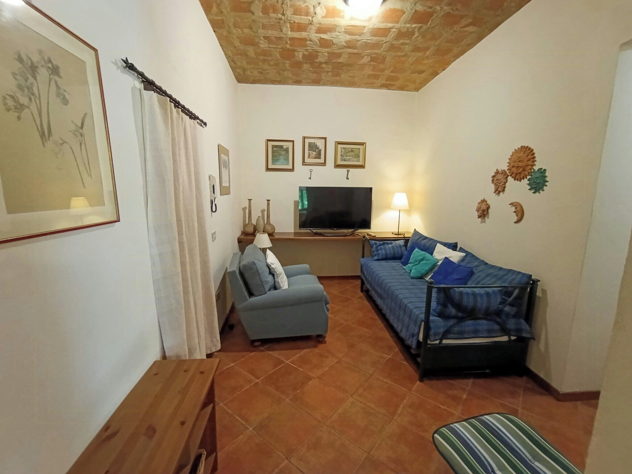 Una sala de estar con un sofá, un televisor, una lámpara y un cuadro en la pared.