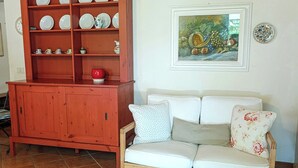 Ein Wohnzimmer mit einer Holzhocker, einem Sofa mit floralen Kissen und einem gerahmten Gemälde an der Wand.