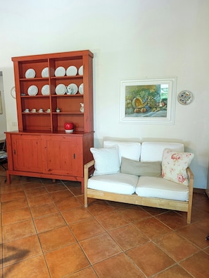Ein Wohnzimmer mit einer Holzhocker, einem Sofa mit floralen Kissen und einem gerahmten Gemälde an der Wand.