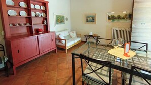 Ein Zimmer mit einem Glastisch, einem roten Schrank mit Geschirr, einem weißen Sofa und zwei Bildern an der Wand.
