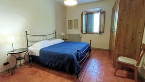 Ein Schlafzimmer mit Bett, Sessel, Tisch, Fenster mit Fensterläden und Heizkörper.