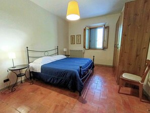 Ein Schlafzimmer mit Bett, Sessel, Tisch, Fenster mit Fensterläden und Heizkörper.