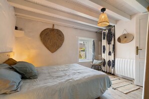 Un dormitorio con una cama, una lámpara colgante, un adorno de pared tejido, una silla y una ventana.