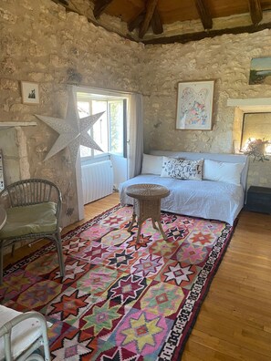 Une pièce rustique avec un mur en pierre, une grande décoration en forme d’étoile, un fauteuil en osier, un tapis à motifs et un lit avec une literie blanche.