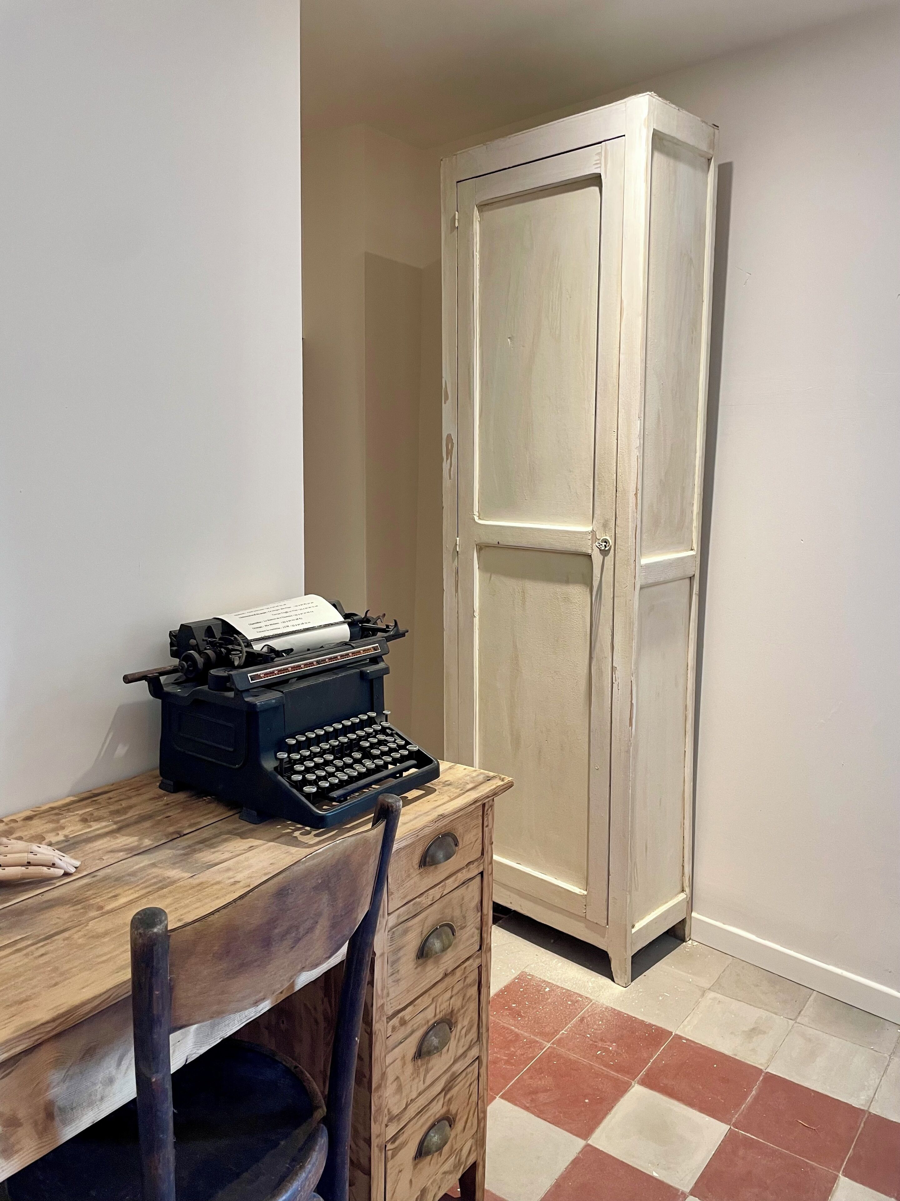 Una stanza con una scrivania in legno, una macchina da scrivere, una sedia, un armadio e un pavimento a scacchi.
