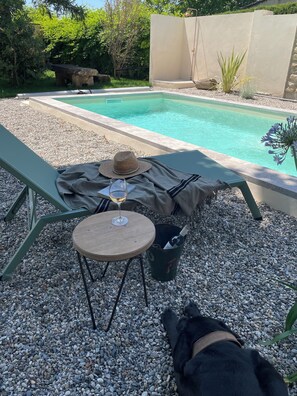 Zona junto a la piscina con una mesa, un sombrero y una copa de vino.