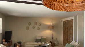 A living room with a sofa, a coffee table, a wicker ceiling light, a television, and a wall with decorative plates. - A house in Provence. (Camaret-sur-Aigues)