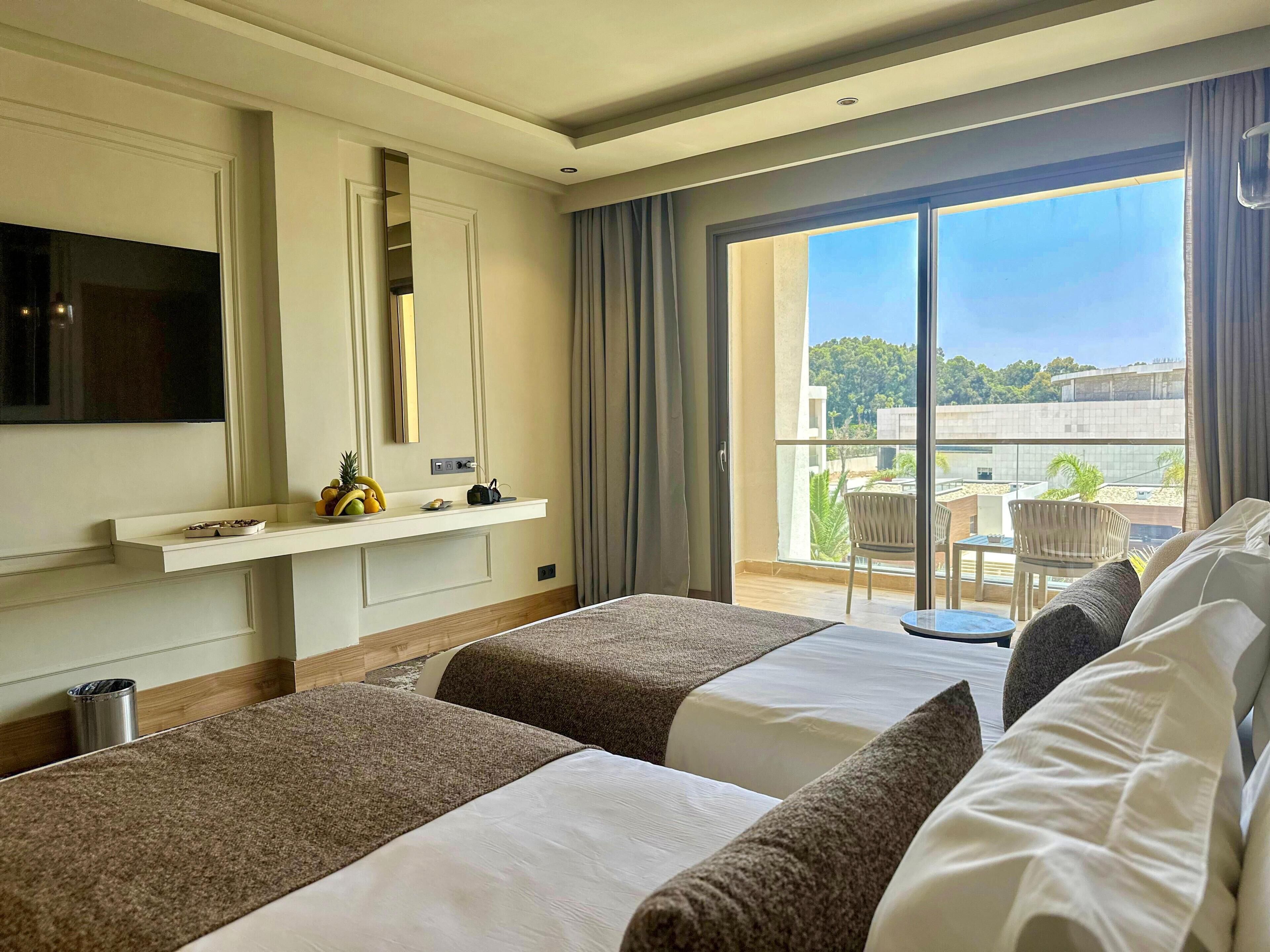 Habitación de hotel con dos camas, televisión, minibar y balcón con vistas.