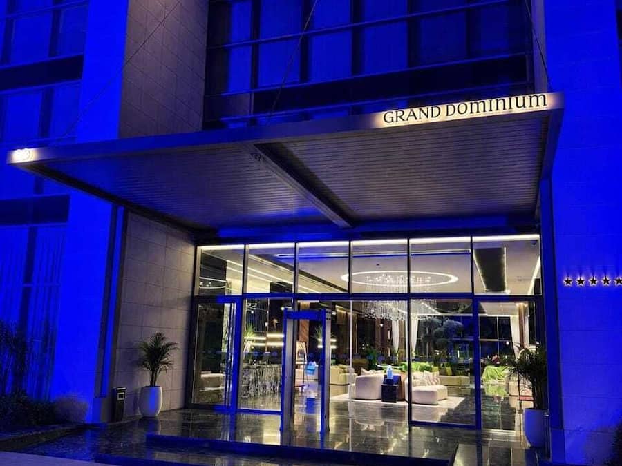 Entrada de un hotel con fachada de vidrio, un letrero que dice 'GRAND DOMINIUM' y un área de acceso cubierta.