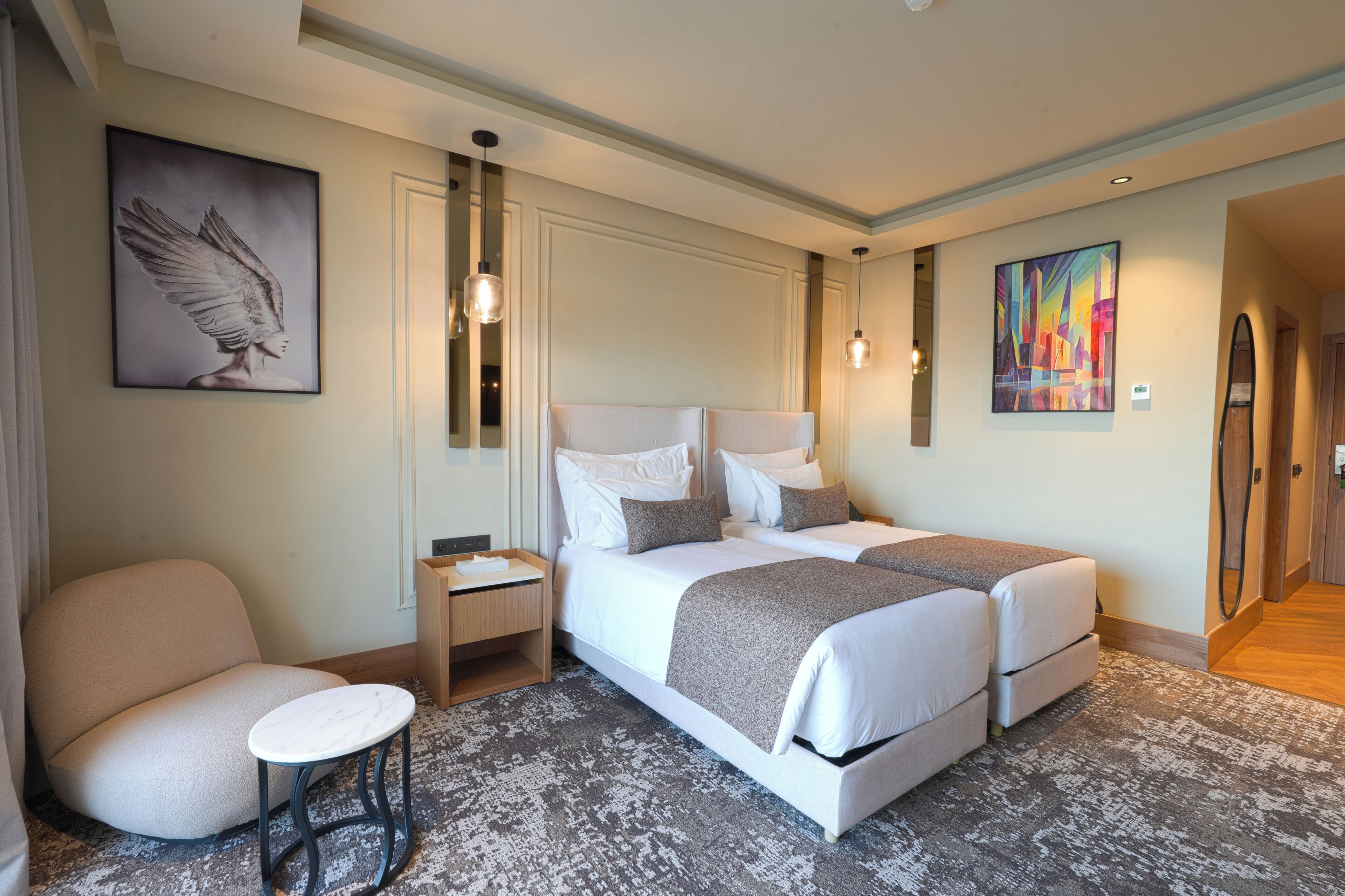 Een hotelkamer met een tweepersoonsbed, nachtkastje, stoel en kunst aan de muur.