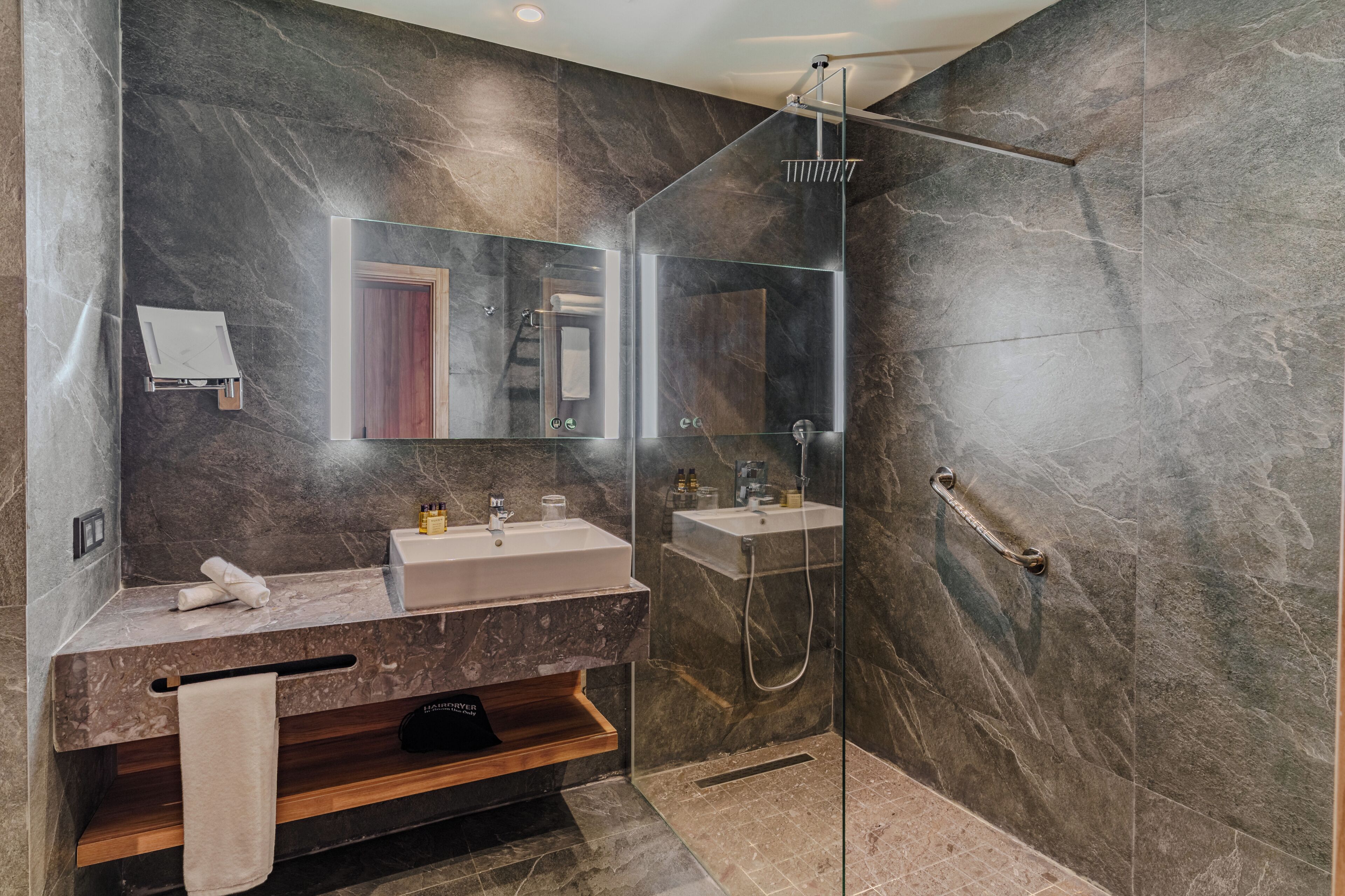 A modern bathroom with a glass shower enclosure, two sinks, and a vanity with a towel rack.