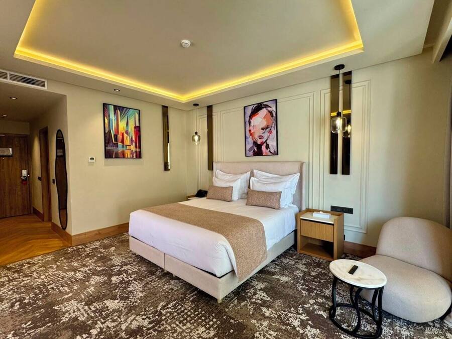 Habitación de hotel con una cama grande, mesitas de noche, una silla y obras de arte en las paredes.