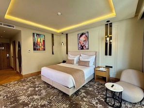 A hotel room with a large bed, bedside tables, a chair, and artwork on the walls. - Grand Dominium (Agadir)