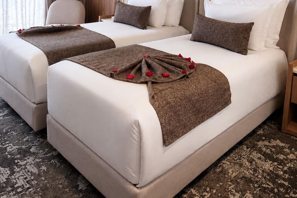 Hotellihuone, jossa on kaksi sänkyä, puuovi, taulu ja moderni valaisin.