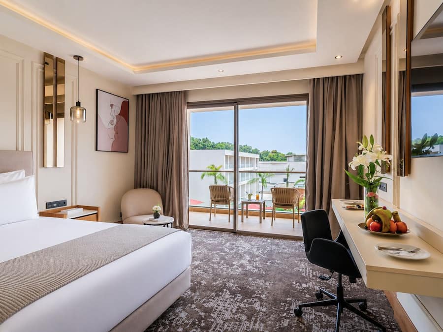 A hotel room with a large bed, a desk, a chair, and a view of the outdoors.