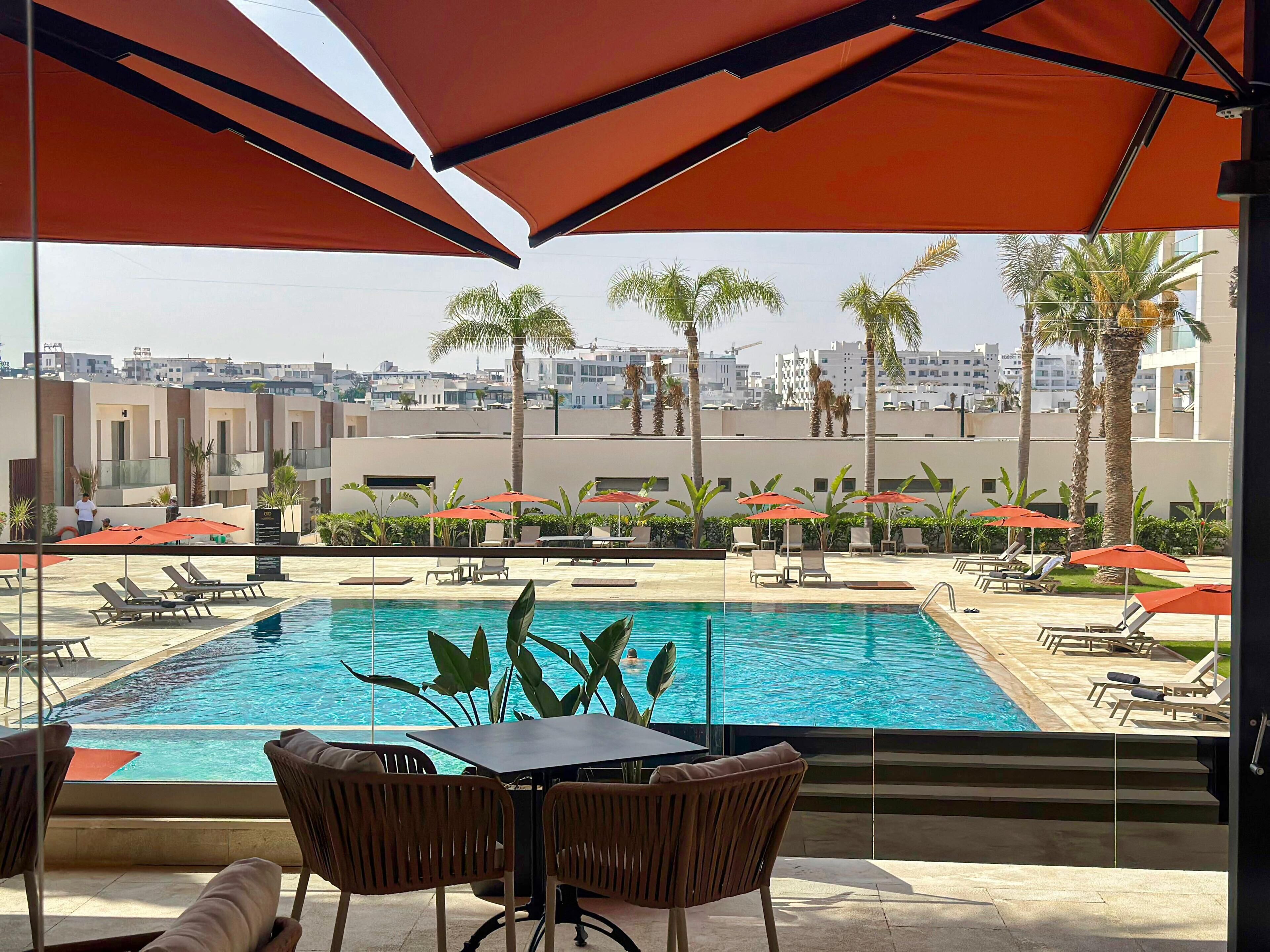 A poolside area with lounge chairs, umbrellas, and a view of buildings in the background.