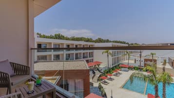 Un balcón de hotel con vista a una piscina, sillas de descanso y una playa.
