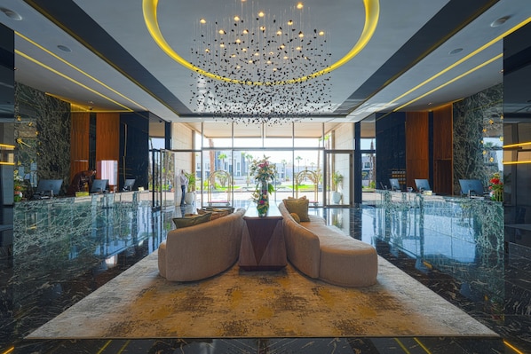 A modern lobby with a central seating area, a chandelier, and a view through large windows. - Grand Dominium (Agadir)