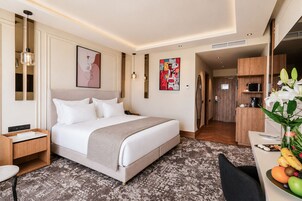 Una camera d'albergo con un letto, un comodino, una lampada, opere d'arte e una scrivania con della frutta.