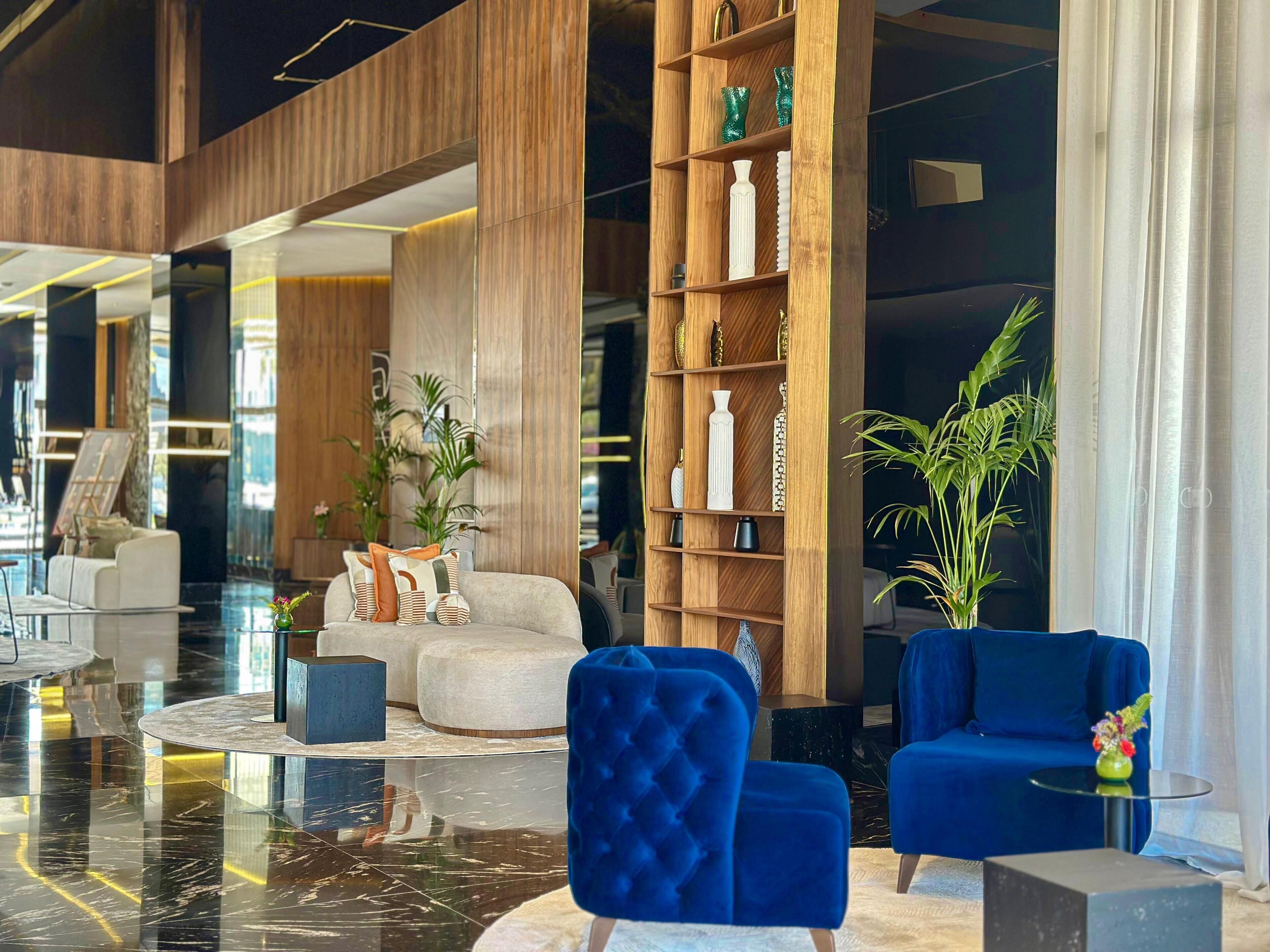 Eine moderne Lobby mit einer Holzbücherwand, einer Sitzecke mit blau-weißen Stühlen und einem großen Spiegel, der den Raum reflektiert.