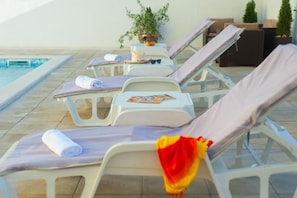 Ein Poolbereich mit Liegestühlen, einem kleinen Tisch mit einem Buch und einer Sonnenbrille sowie einem Blumentopf.