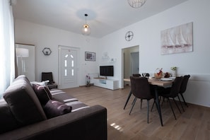 Ein modernes Wohnzimmer mit einer Couch, einem Fernseher, einem Esstisch, Stühlen und Kunstwerken an den Wänden.