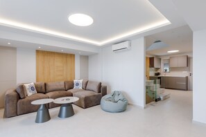 Ein modernes Wohnzimmer mit einer Couch, zwei runden Tischen, einem Sitzsack und einer Küchenzeile mit Schränken sowie einer Treppe.