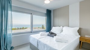 Une chambre à coucher avec un lit, une table de chevet, un ventilateur de plafond et une grande fenêtre avec des rideaux.