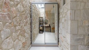 Un stretto corridoio in pietra con una porta specchiata che conduce a una stanza con un letto e un tavolino.