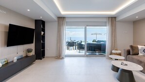 Un soggiorno moderno con televisione a schermo piatto, un divano, due tavolini da caffè e un balcone con mobili da esterno.