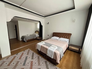 Un dormitorio con una cama grande, una cama más pequeña, una alfombra estampada y suelo de madera.