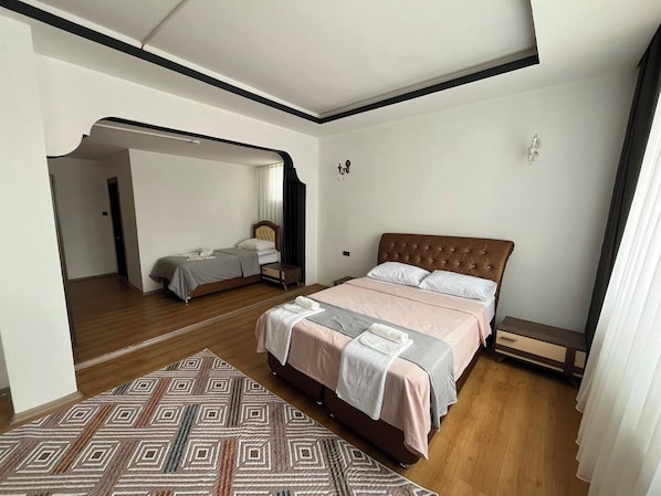 Ein Schlafzimmer mit einem großen Bett, einem kleineren Bett, einem gemusterten Teppich und Holzboden.
