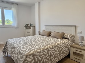 A bedroom with a bed, bedside tables, a nightstand, a dresser, and a window with curtains.