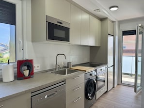 A modern kitchen with a dishwasher, washing machine, microwave, and a coffee maker. - Apartment Los Jazmines 20002 (Santiuste)