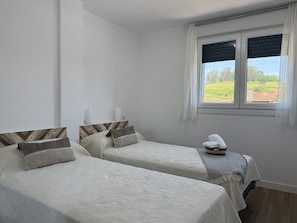A room with two beds, a window with curtains, and a view of greenery outside. - Apartment Los Jazmines 20002 (Santiuste)