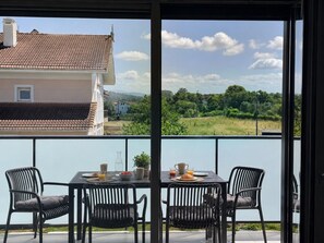 Un balcon avec une table préparée pour le petit-déjeuner, donnant sur un quartier résidentiel et un espace verdoyant.