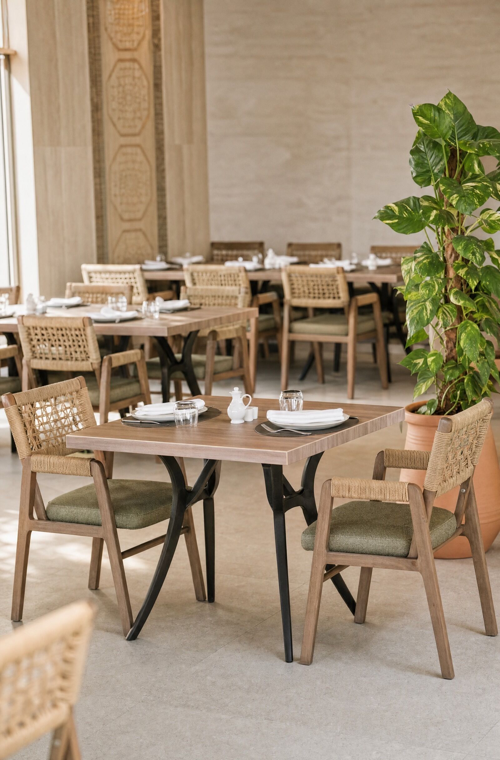 A dining area with wooden tables and chairs, a potted plant, and a tiled floor.