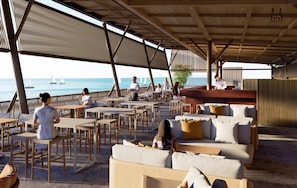 A covered outdoor seating area with tables and chairs, overlooking the sea with sailboats in the distance. - CHAONIAN Hotel (Himare)