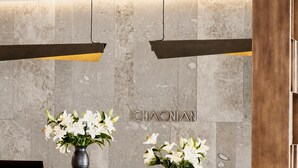 A reception area with a marble wall, two flower vases, a wooden reception desk, and a pair of chairs. - CHAONIAN Hotel (Himare)