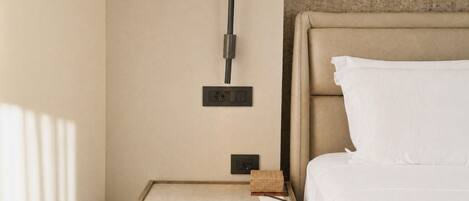 A hotel room with a bed, a nightstand, a wall-mounted light, and a power outlet.